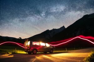 A van with bikes parked under a star-filled sky and mountains, creating a peaceful night scene.